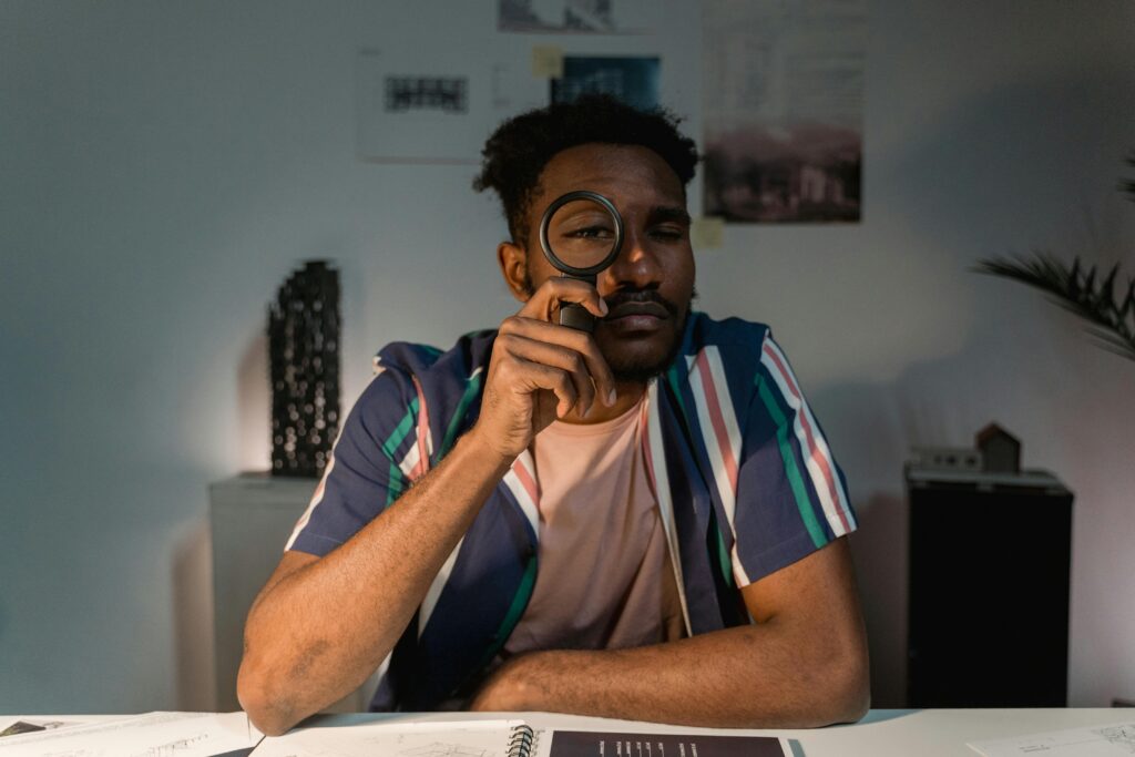 A contemplative man holding a magnifying glass at a table indoors.